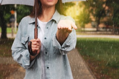 Photo of Young woman with umbrella walking under rain in park, closeup