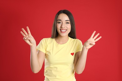 Photo of Woman in yellow t-shirt showing number six with her hands on red background