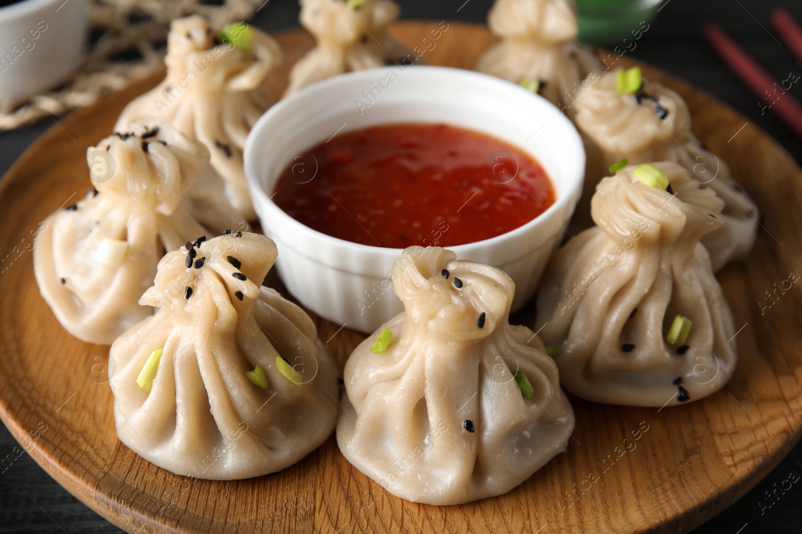 Photo of Wooden plate with tasty baozi dumplings and sauce, closeup