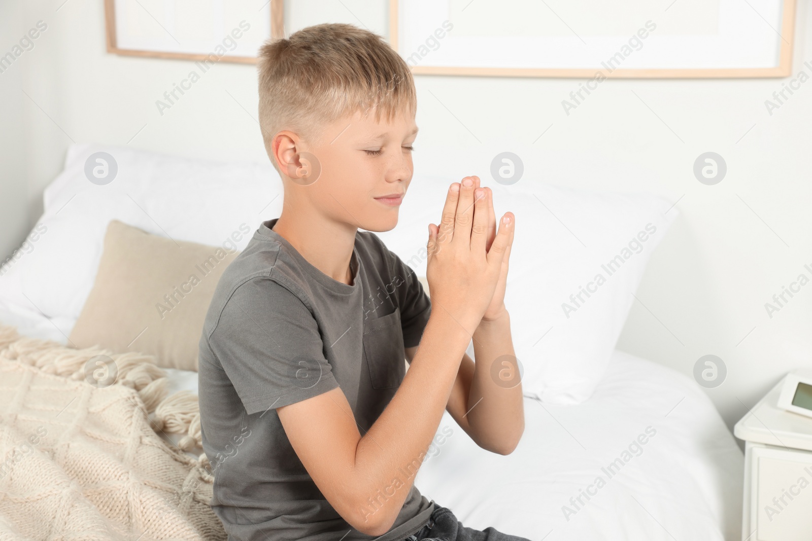 Photo of Boy with clasped hands praying on bed at home