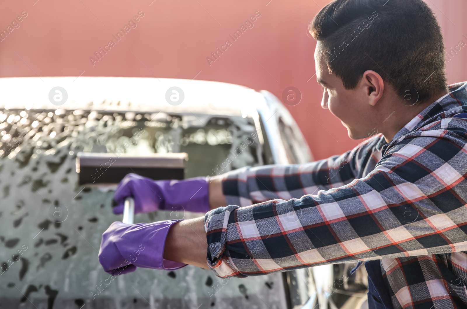 Photo of Worker cleaning automobile window with squeegee at car wash