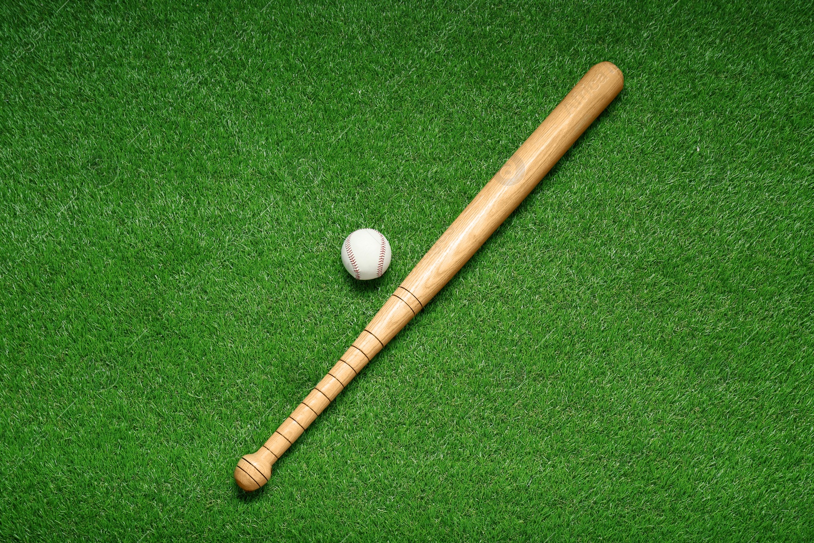 Photo of Wooden baseball bat and ball on green grass, flat lay. Sports equipment