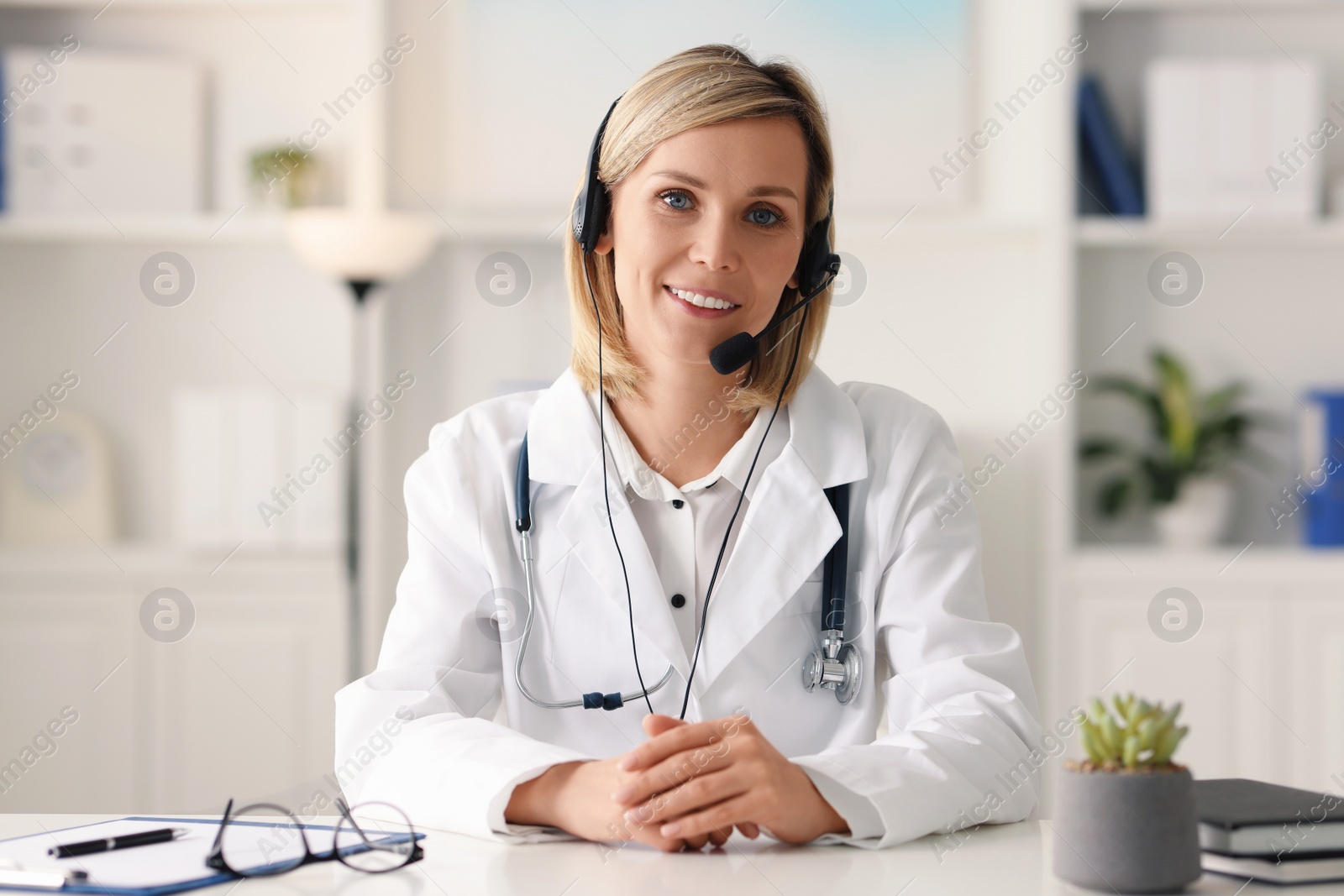 Photo of Portrait of smiling doctor in headphones having online consultation at table indoors