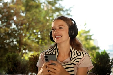Photo of Smiling woman in headphones using smartphone outdoors