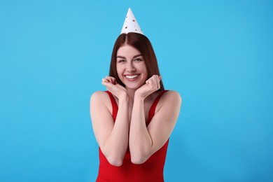 Happy woman in party hat on light blue background