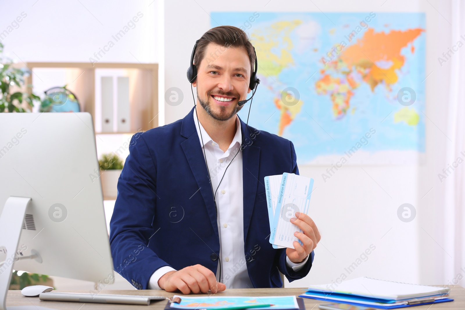 Photo of Male consultant with headset holding tickets in travel agency