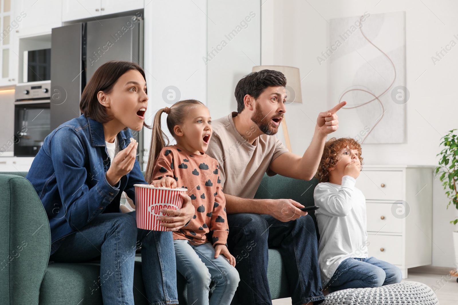 Photo of Surprised family watching TV with popcorn on sofa at home