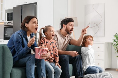 Photo of Surprised family watching TV with popcorn on sofa at home