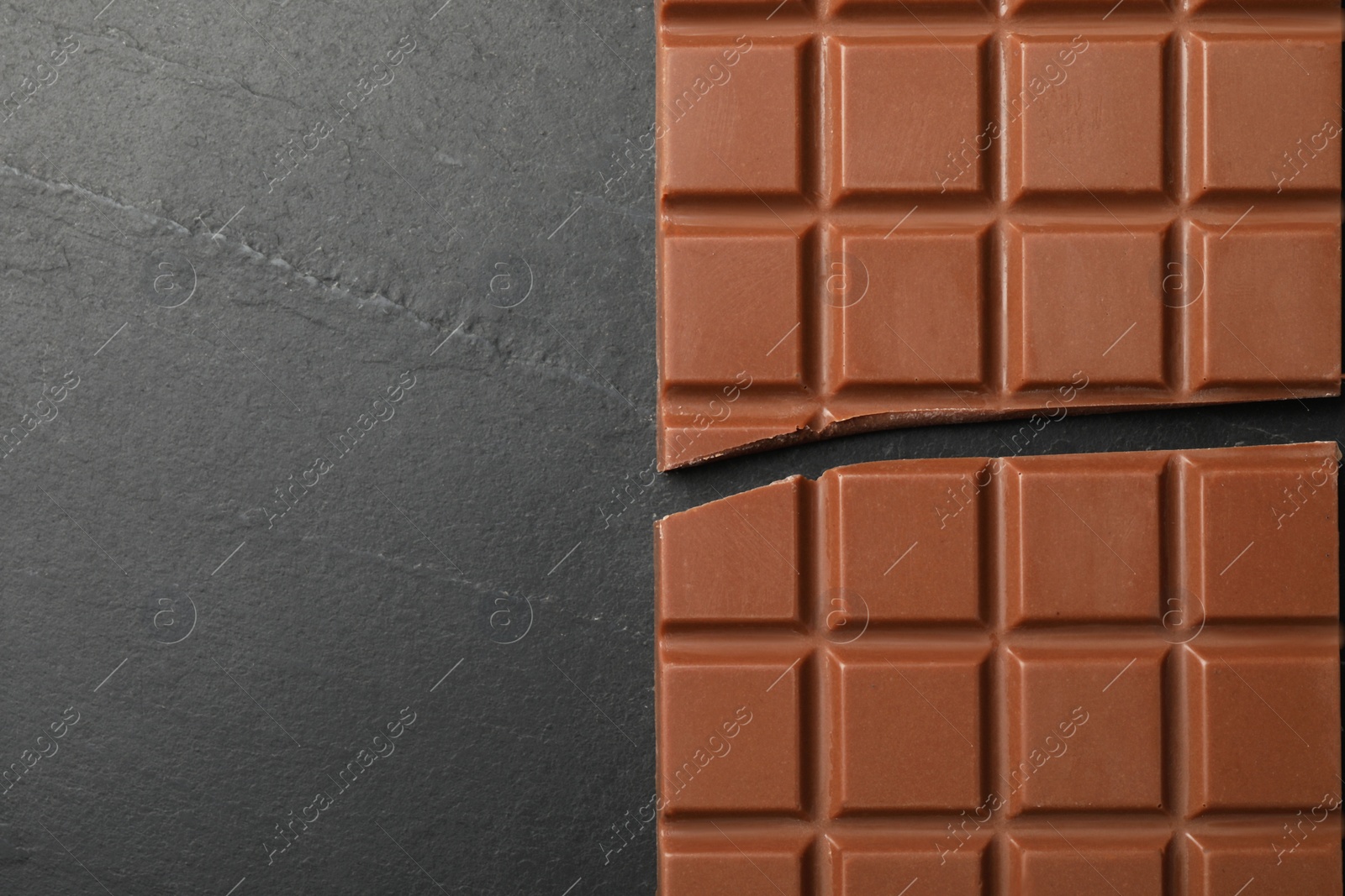 Photo of Tasty broken chocolate bar on grey table, top view. Space for text