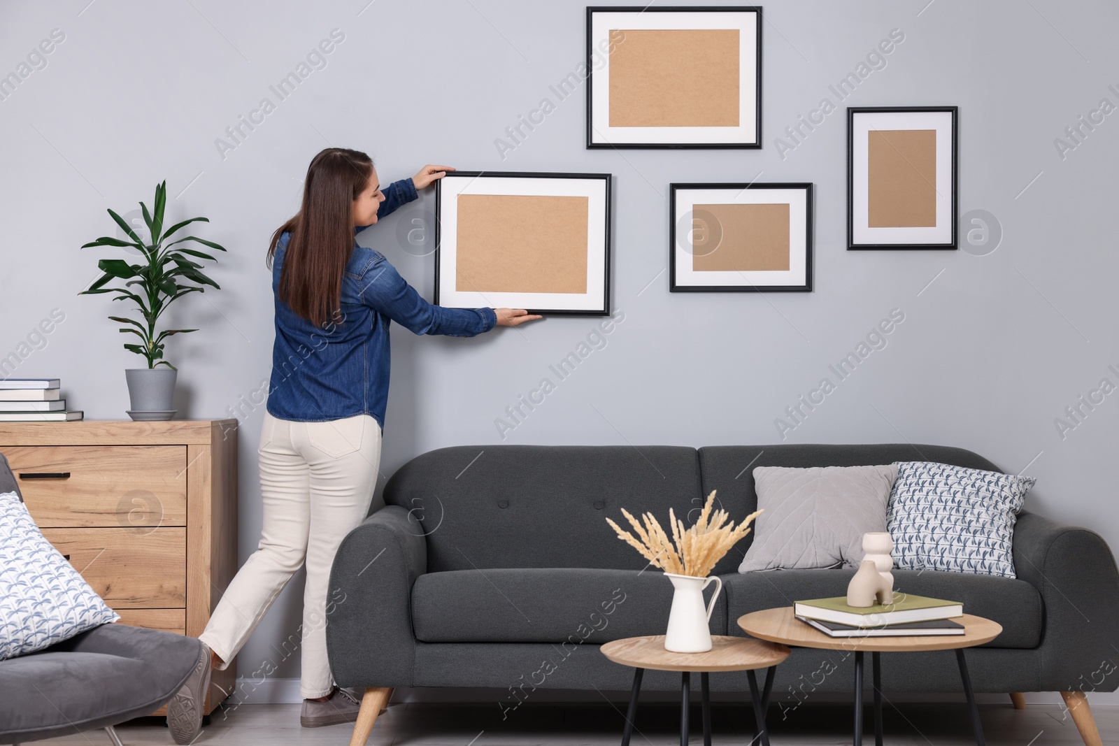 Photo of Woman hanging picture frame on gray wall at home