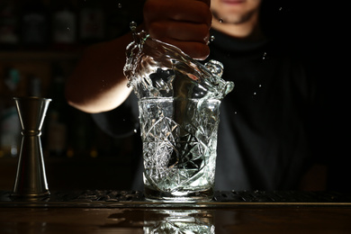 Photo of Bartender preparing fresh alcoholic cocktail at bar counter, focus on glass