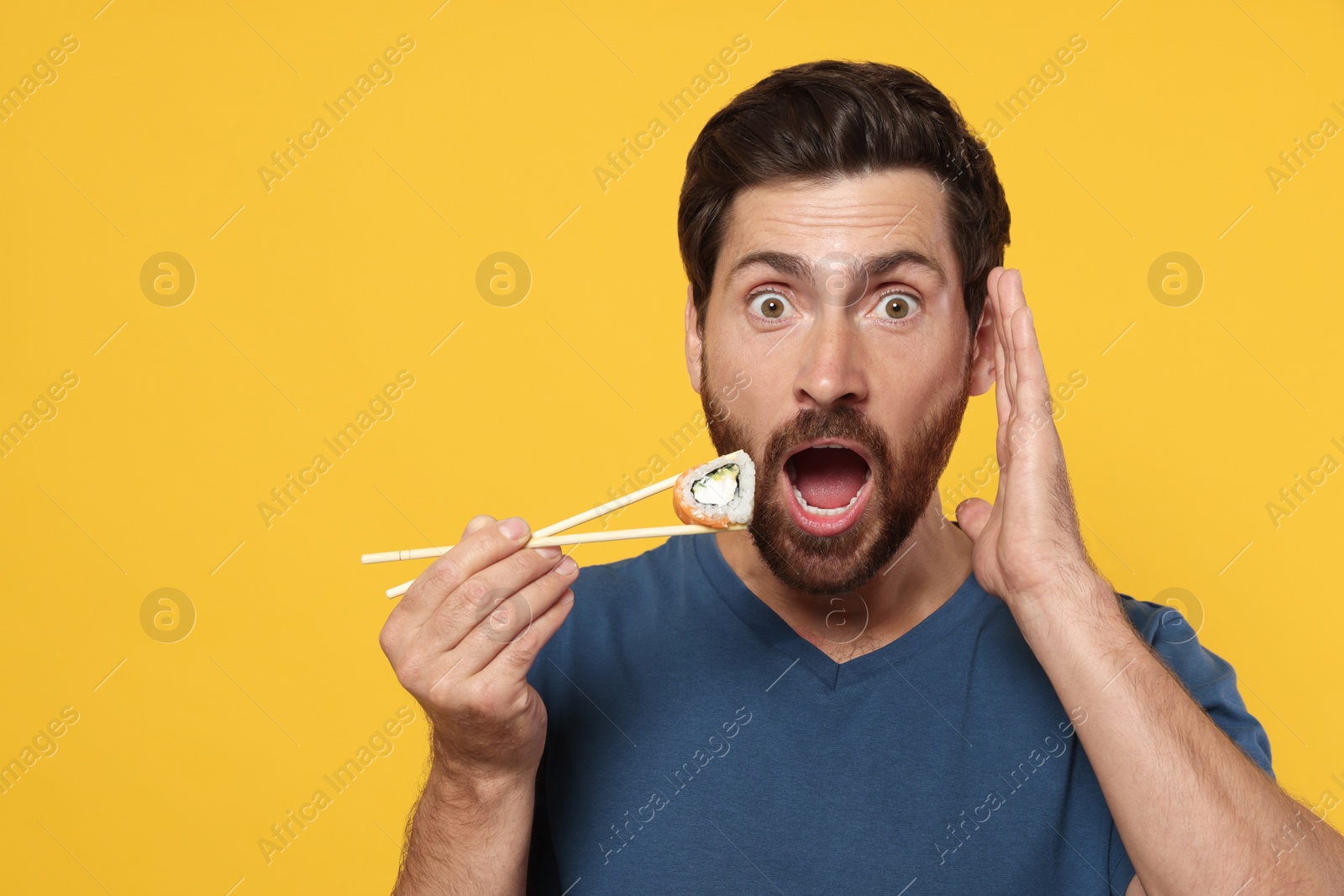 Photo of Emotional man holding sushi roll with chopsticks on orange background. Space for text