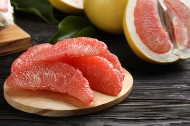 Photo of Peeled pomelo slices on black wooden table, closeup