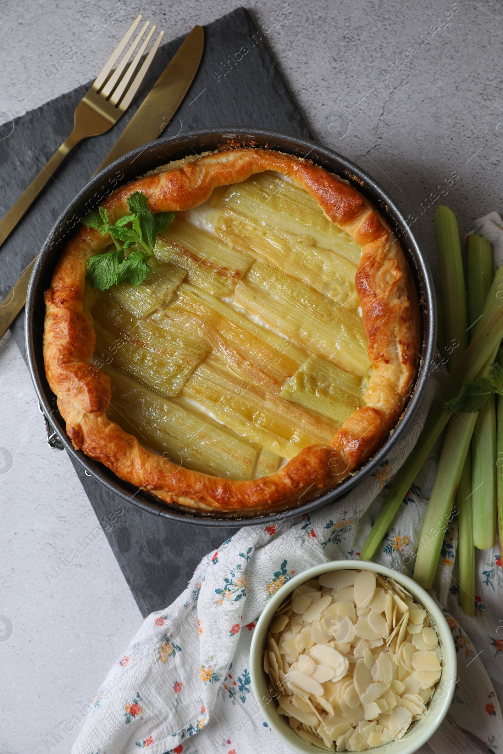 Photo of Freshly baked rhubarb pie, stalks and cutlery on light grey table, flat lay