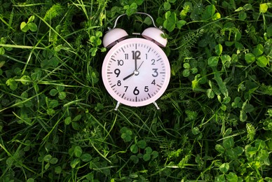 Pink small alarm clock on green grass outdoors, top view. Space for text