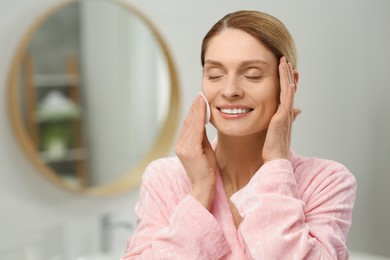 Photo of Beautiful woman removing makeup with cotton pad indoors, space for text