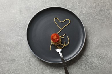 Photo of Heart made of tasty spaghetti, fork and tomato on light grey table, top view