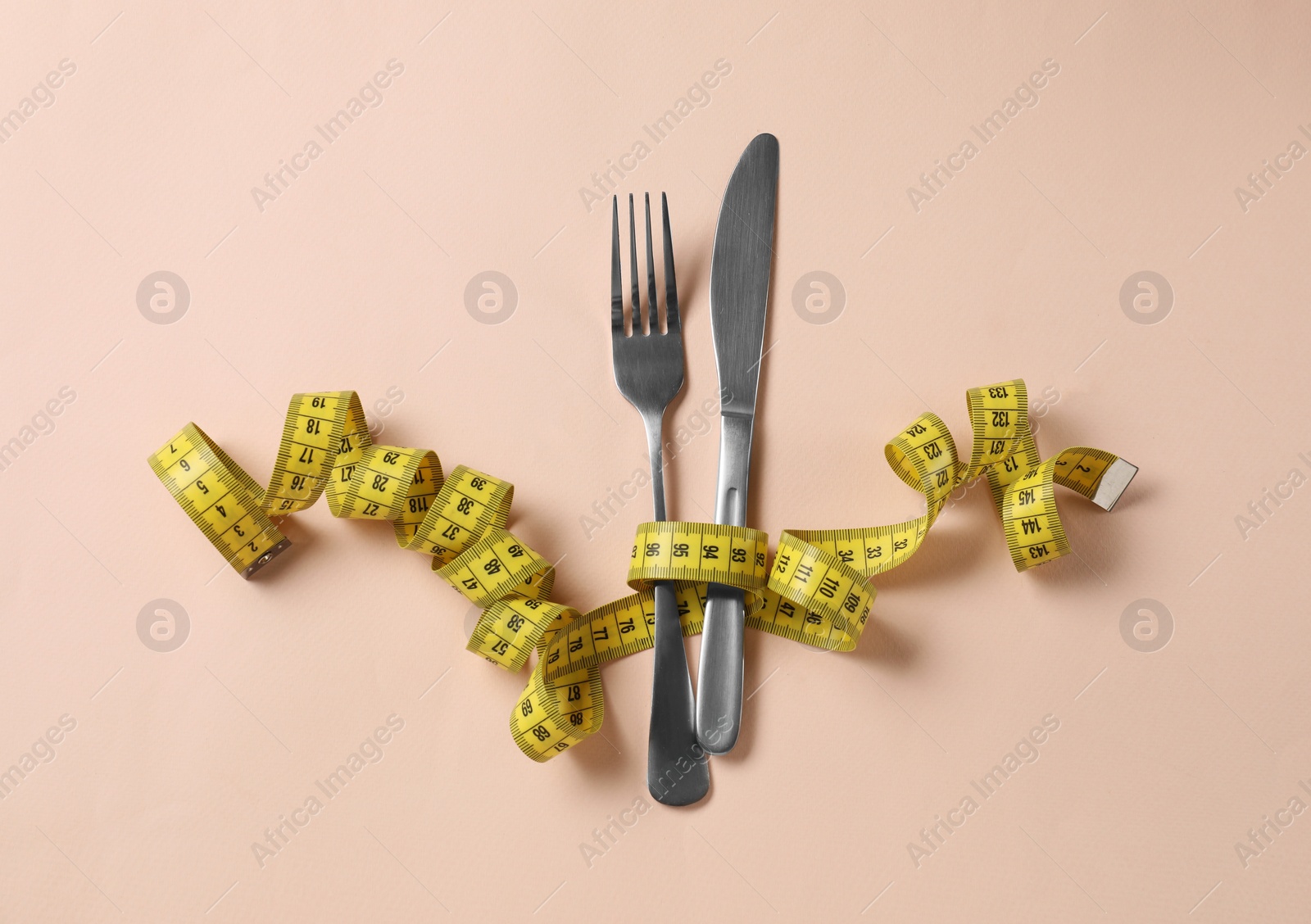 Photo of Fork. knife and measuring tape on beige background, flat lay. Diet concept