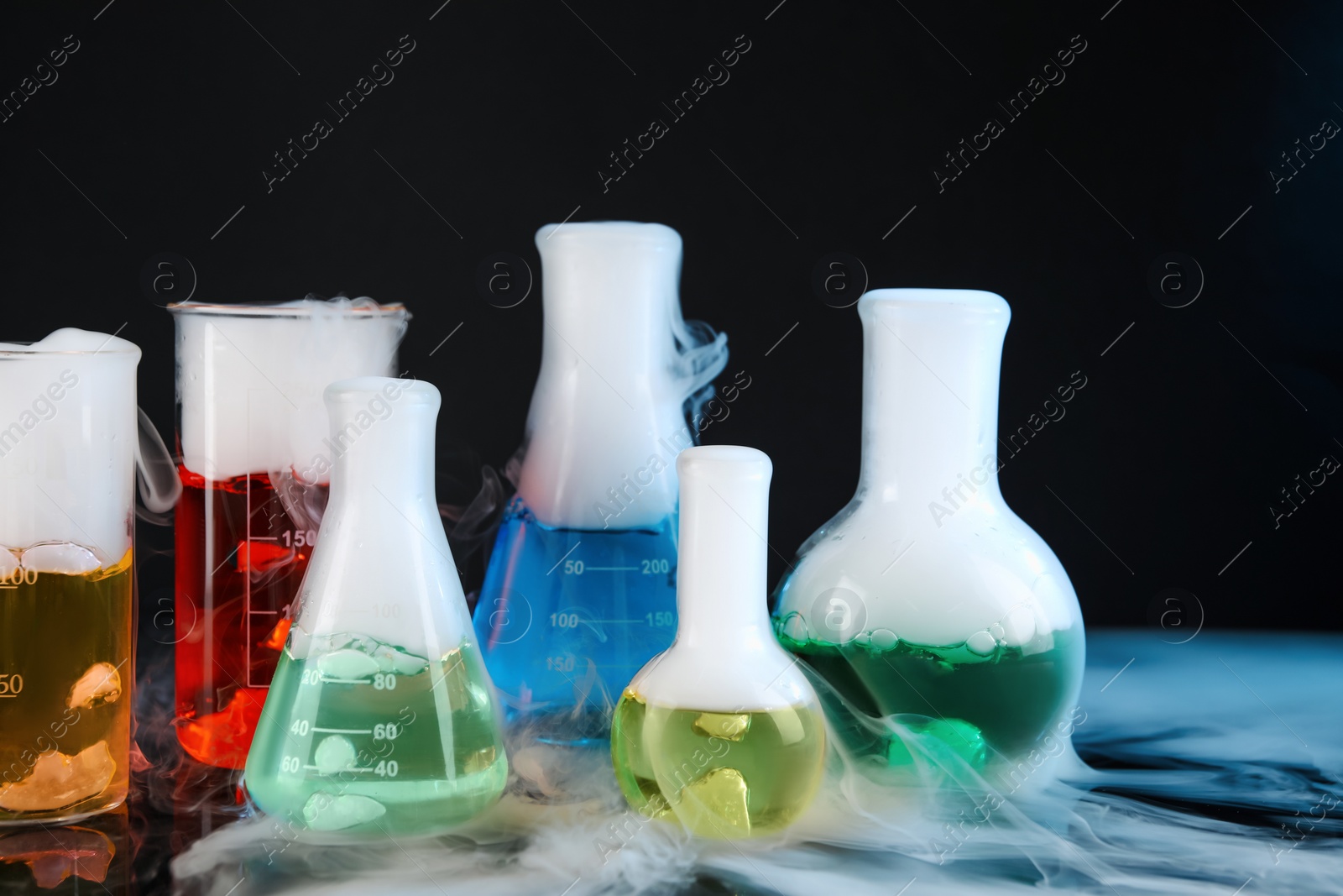 Photo of Laboratory glassware with colorful liquids and steam on black background. Chemical reaction