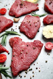 Photo of Fresh raw meat steaks and spices on light grey table