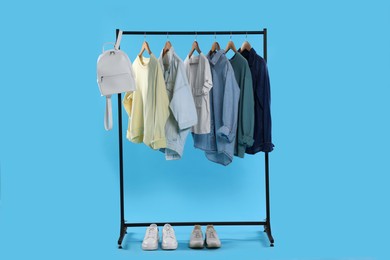 Photo of Rack with accessories and stylish clothes on wooden hangers against light blue background