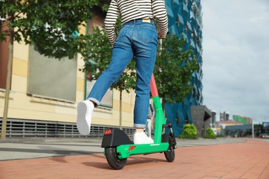 Photo of Woman riding modern electric kick scooter on city street, back view