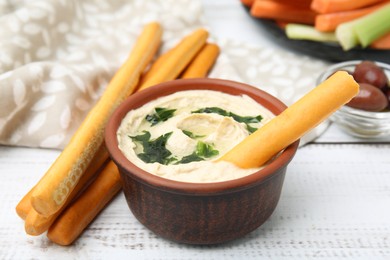 Photo of Delicious hummus with grissini sticks on white wooden table