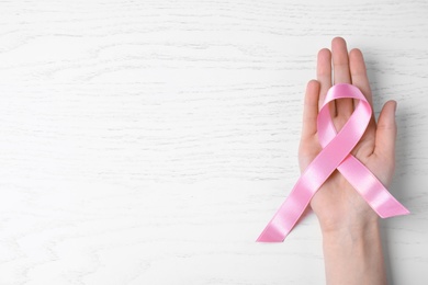 Photo of Woman with symbolic ribbon of breast cancer awareness and space for text on white wooden background, top view. Gynecological care