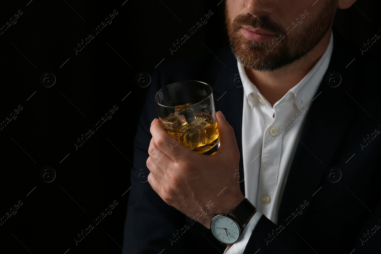 Photo of Man holding glass of whiskey with ice cubes on black background, closeup