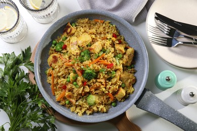 Tasty rice with meat and vegetables in frying pan served on white table, flat lay