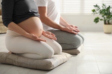 Young pregnant woman with her husband practicing yoga at home, closeup