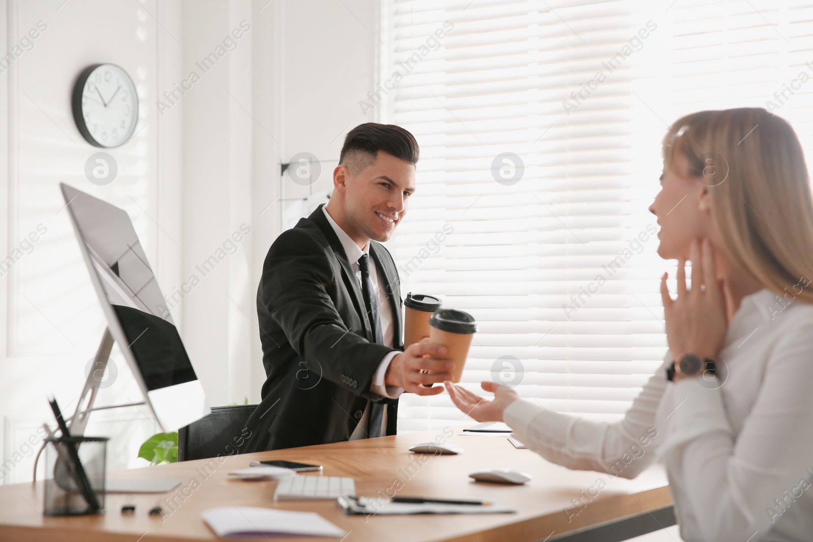 Photo of Man giving cup of coffee to his colleague in office. Flirting at work