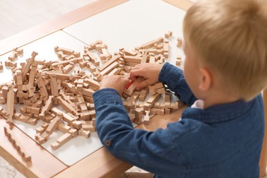 Photo of Little boy playing with wooden blocks at table indoors. Child's toy