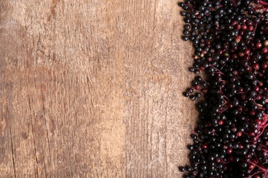 Photo of Tasty elderberries (Sambucus) on wooden table, top view. Space for text