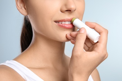 Photo of Young woman applying balm on her lips against color background, closeup