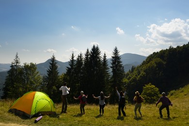 Group of happy tourists near camping tent in mountains, back view