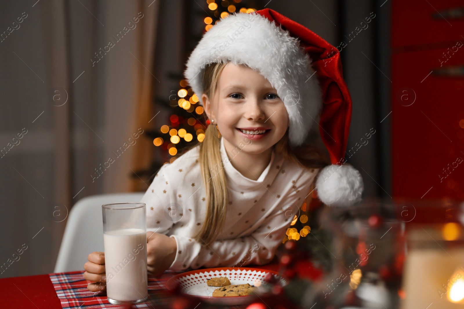 Photo of Cute little child with milk and cookies at table in dining room. Christmas time