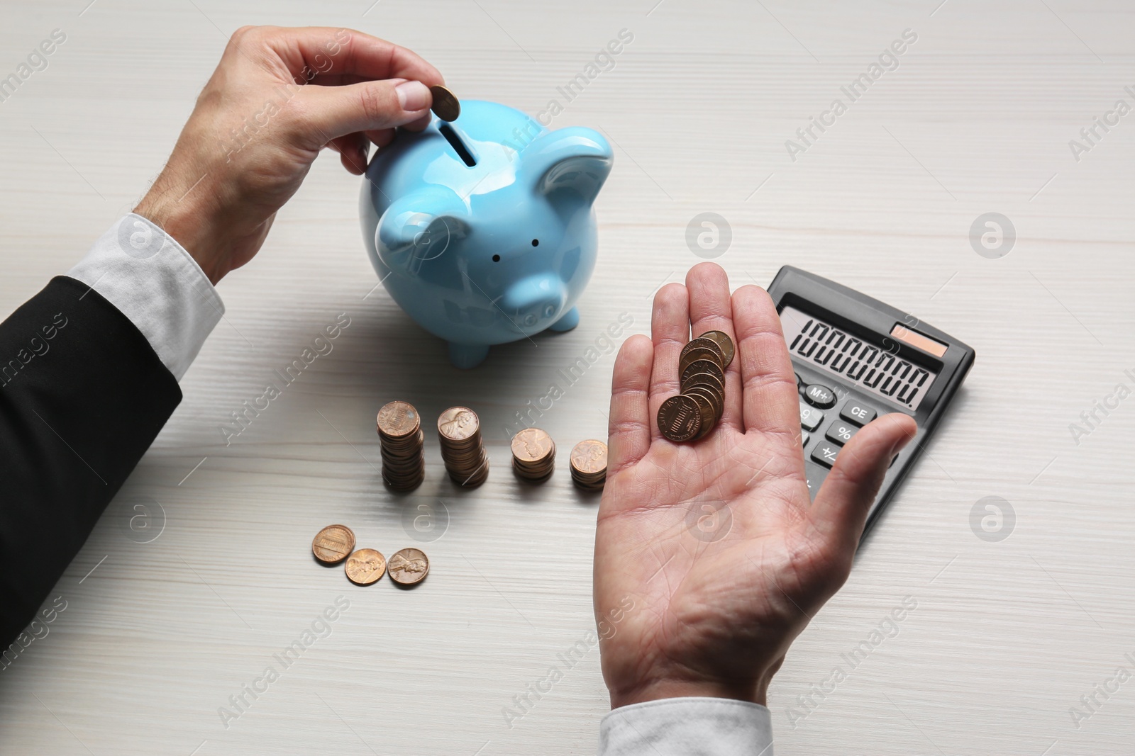 Photo of Budget planning. Businessman putting coin into piggy bank at light wooden table, closeup