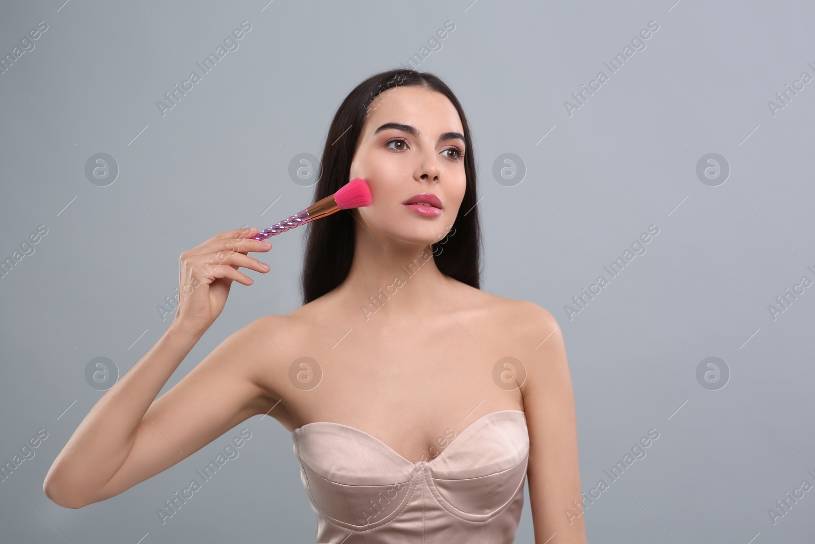 Photo of Woman applying makeup with brush on light grey background