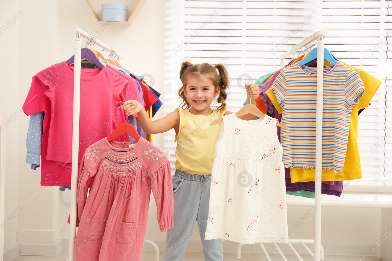 Photo of Little girl choosing clothes on racks indoors