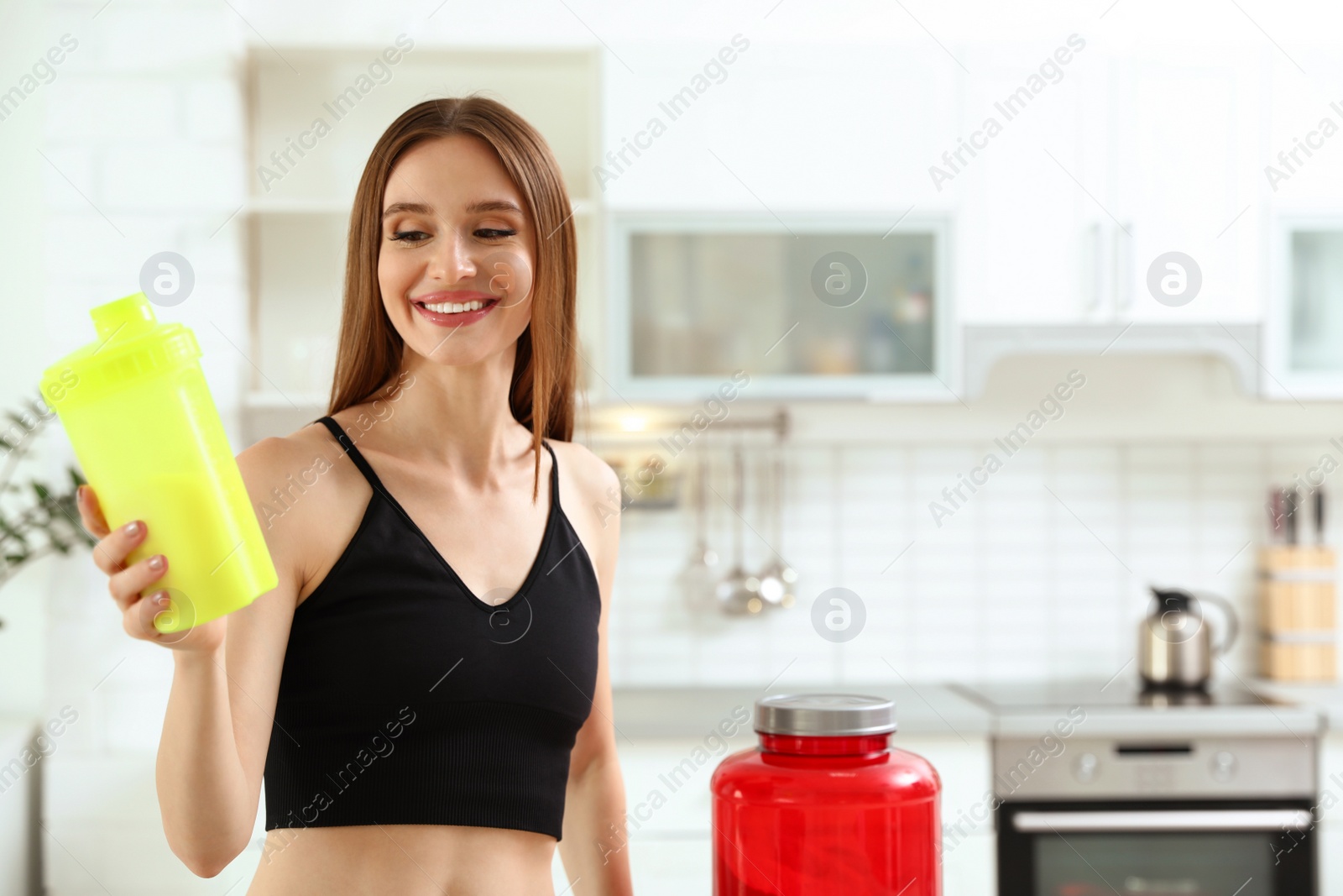 Photo of Young woman with bottle of protein shake in kitchen. Space for text