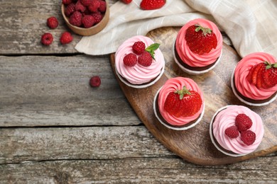 Photo of Sweet cupcakes with fresh berries on wooden table, flat lay. Space for text