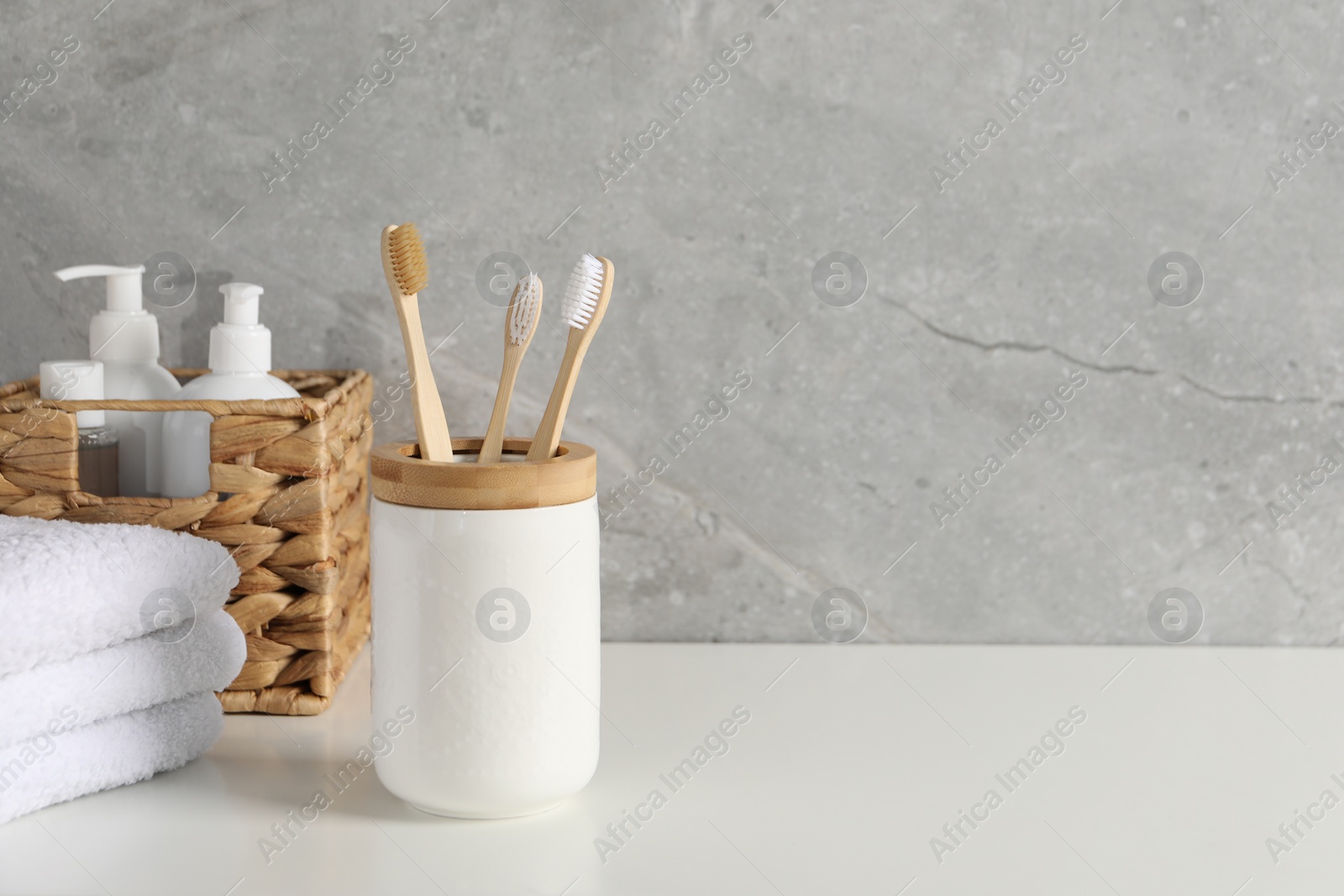 Photo of Bamboo toothbrushes in holder, towels and cosmetic products on white countertop, space for text