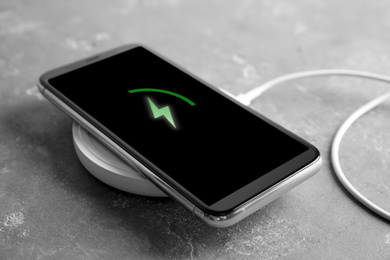 Photo of Mobile phone charging with wireless pad on grey stone table, closeup