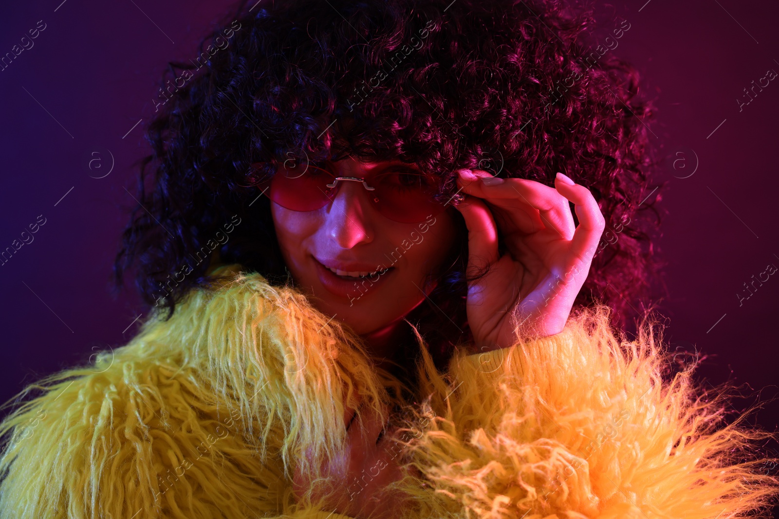 Photo of Beautiful young woman in yellow fur coat and sunglasses on color background in neon lights