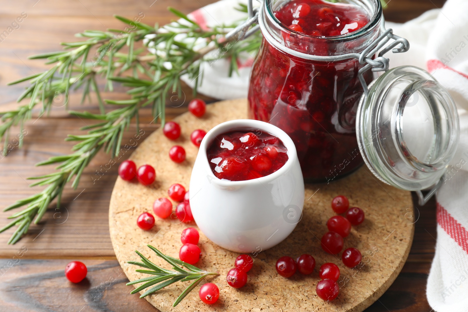 Photo of Cranberry sauce, fresh berries and rosemary on wooden table