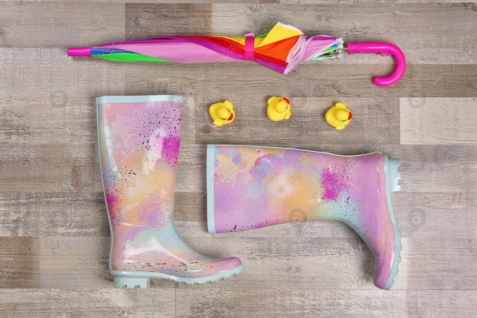 Photo of Pair of gumboots and umbrella on wooden background, top view. Female shoes