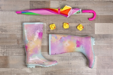 Photo of Pair of gumboots and umbrella on wooden background, top view. Female shoes