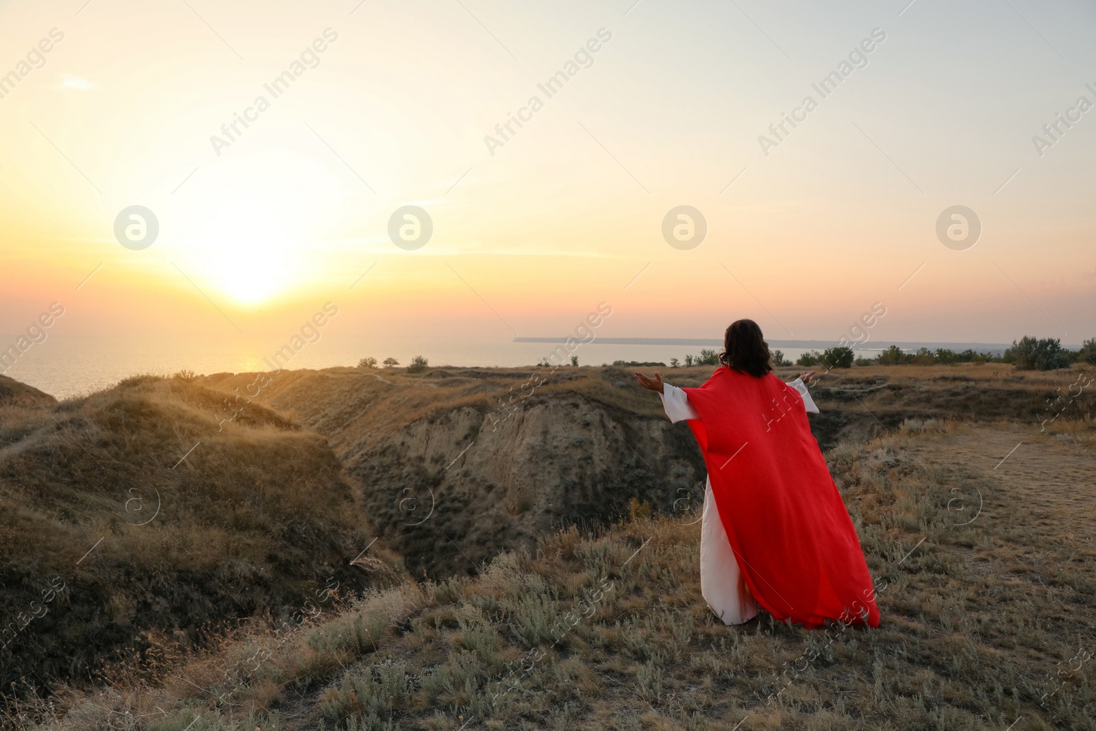 Photo of Jesus Christ raising hands on hills at sunset, back view. Space for text