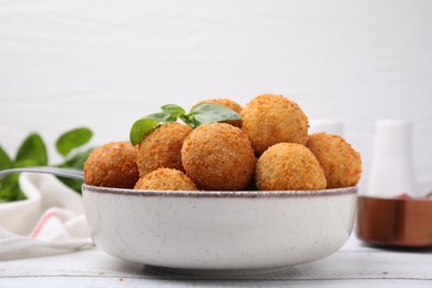 Photo of Bowl of delicious fried tofu balls with basil on white wooden table